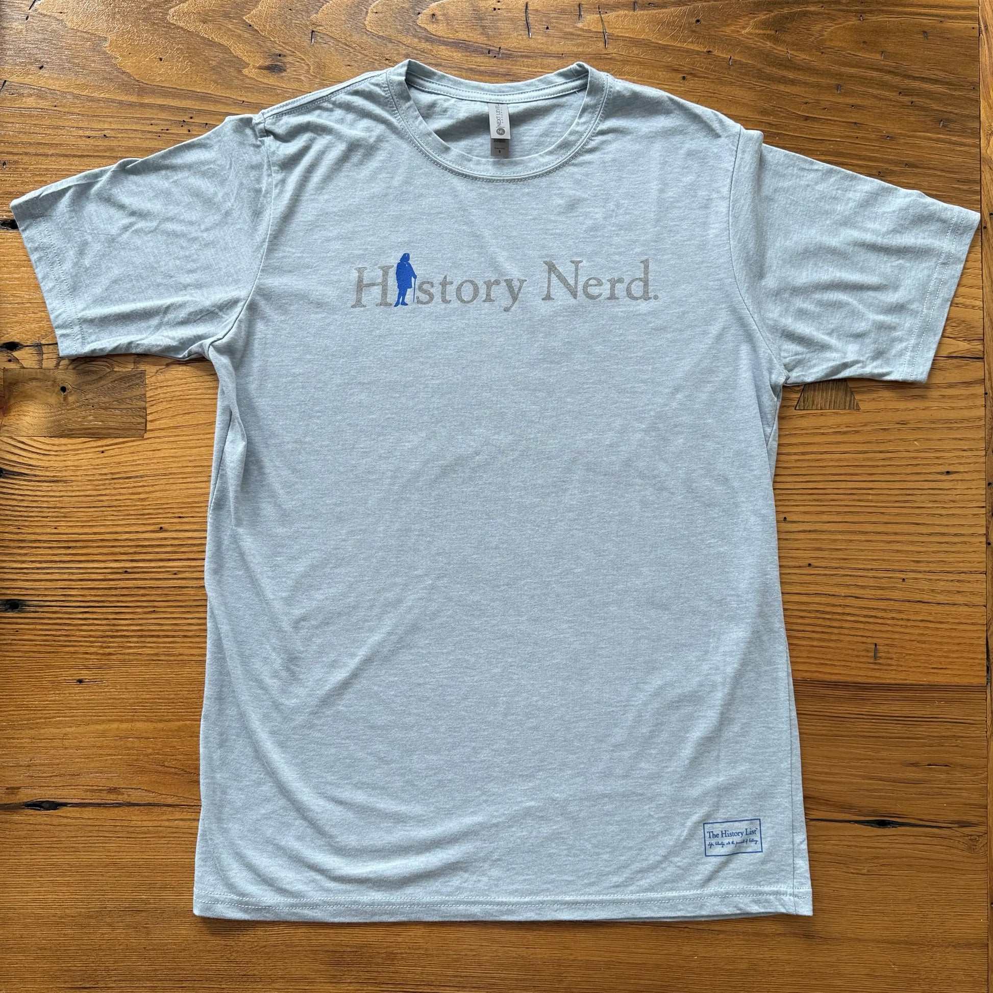 Light blue heather t-shirt with 'History Nerd' text and logo on a wooden surface from The History List store