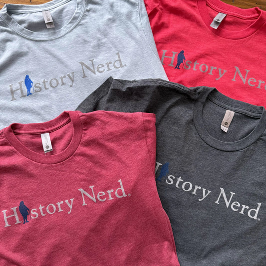 Four 'History Nerd' t-shirts in gray, red, and blue on a wooden surface from The History List store
