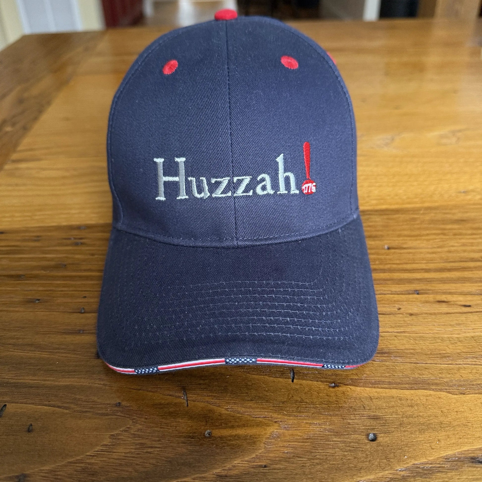 Navy blue cap with 'Huzzah!' text on a wooden surface from The History List store
